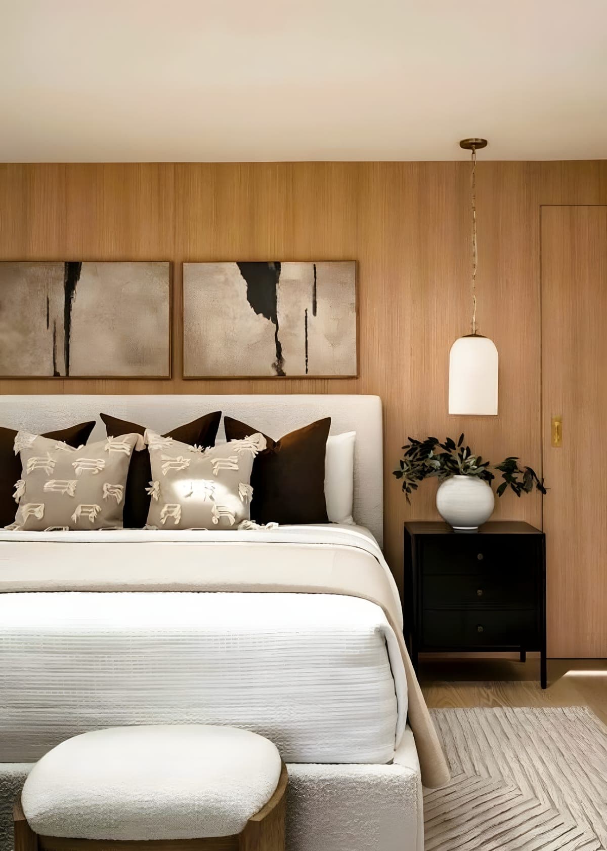 Bedroom accent wall with white oak paneling, abstract diptych artwork, pendant light, and a boucle ottoman