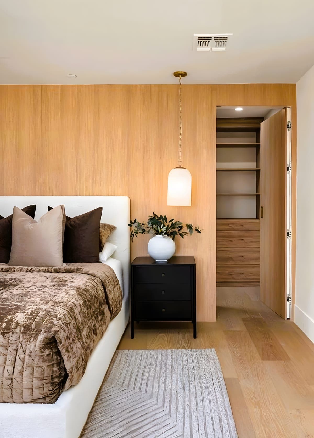 Bedroom wall with white oak paneling, a pendant light, and a walk-in closet entry