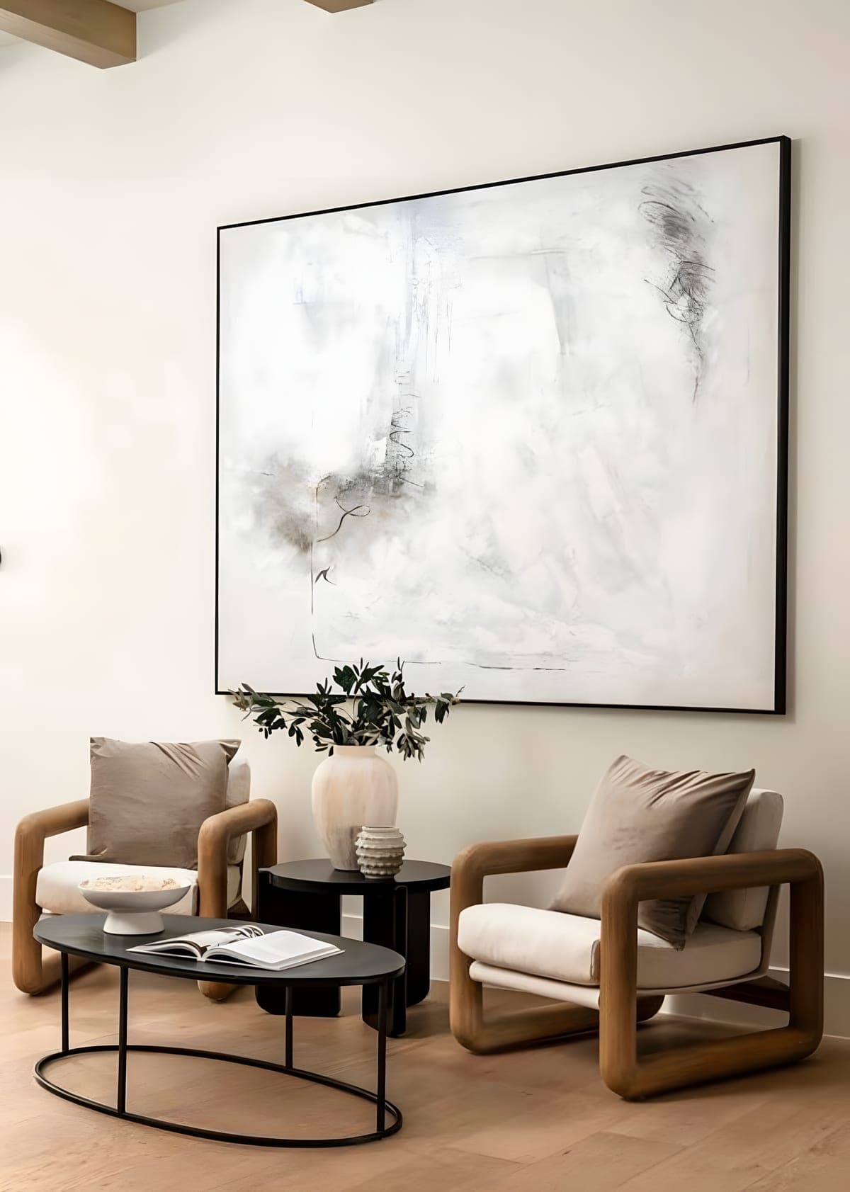 Entry seating area with sculptural wood-frame chairs, a large abstract painting, black oval coffee table, and exposed wood beam ceiling