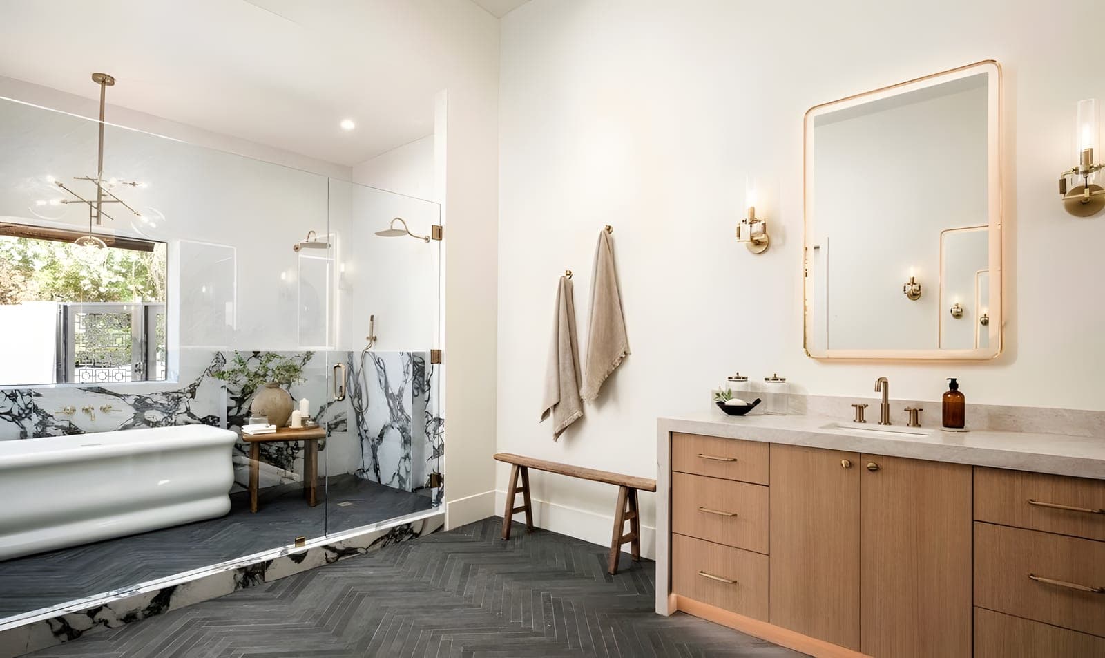 Guest bath with calacatta viola marble walls in a wet room area, brass rain shower and wall-mount faucet, herringbone tile floor, white oak vanity with brass-framed mirror