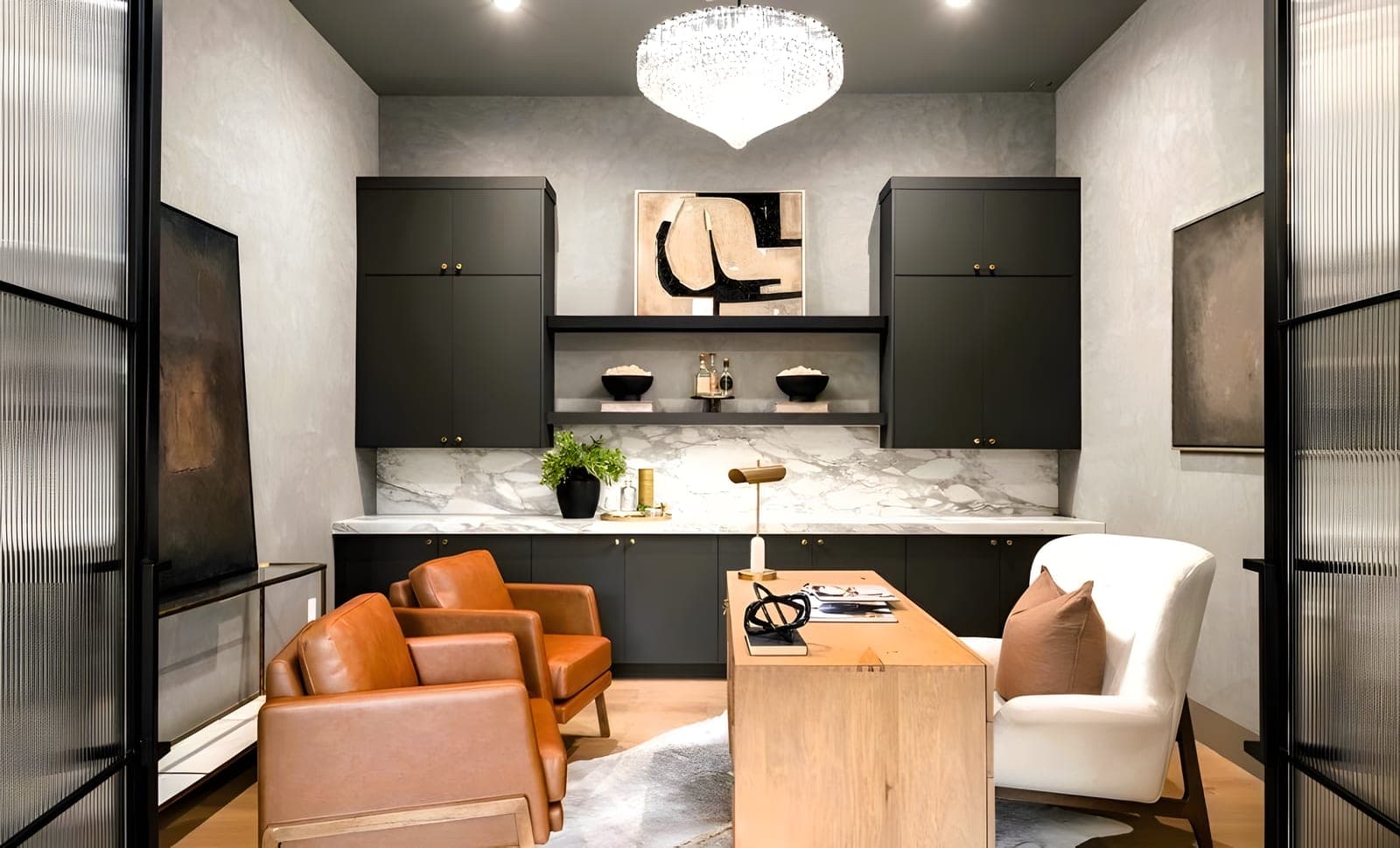 Home office with dark-painted custom cabinetry, calacatta marble backsplash, crystal chandelier, cognac leather chairs, and fluted glass partition doors